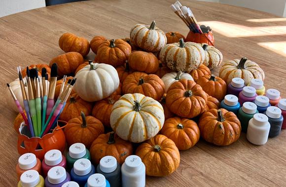 Multiple pumpkins on table with paint and brushes.